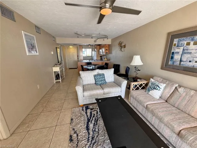 Living area with light tile patterned floors, a textured wall, a textured ceiling, and a ceiling fan