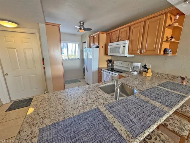 Kitchen with white appliances, light tile patterned flooring, open shelves, ceiling fan, and light stone countertops