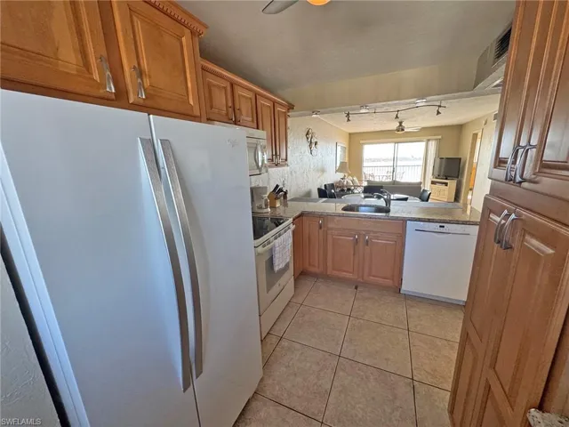 Kitchen featuring white appliances, brown cabinetry, light tile patterned floors, and open floor plan