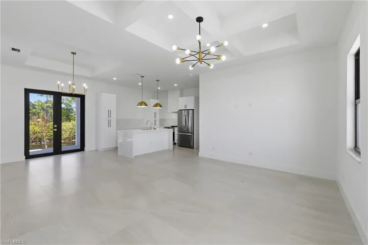 Unfurnished living room featuring hanging lights, coffered ceiling, and french doors