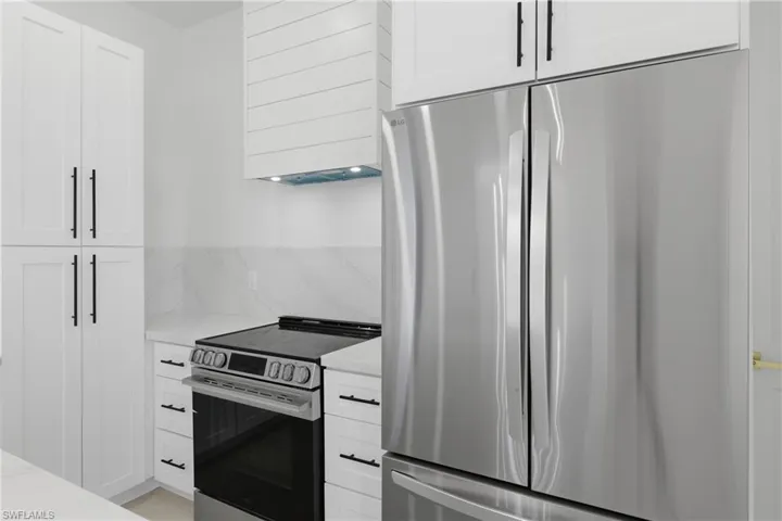 Kitchen with stainless steel appliances, white cabinets, light stone countertops, and backsplash