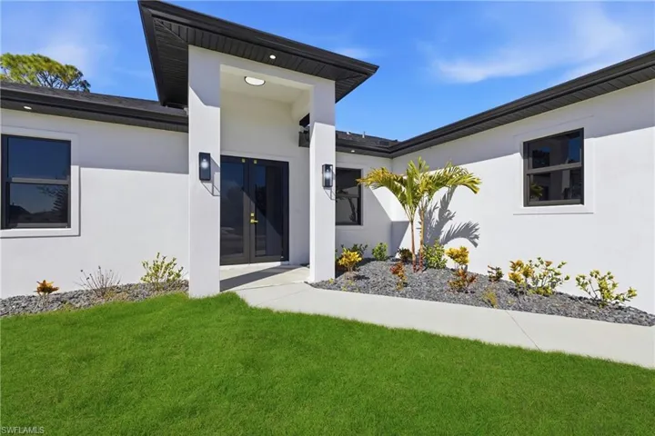 Entrance to property featuring stucco siding, french doors, and a lawn