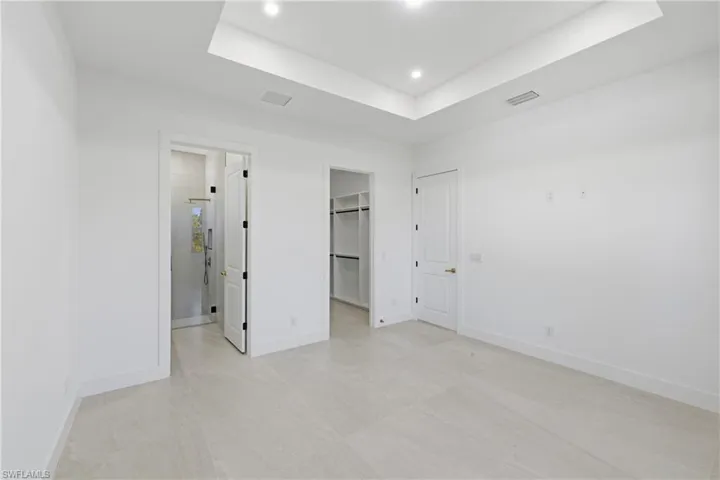 Unfurnished bedroom featuring a spacious closet, a raised ceiling, and recessed lighting