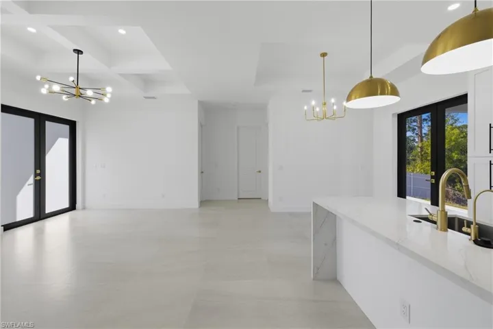 Kitchen featuring french doors, hanging lights, coffered ceiling, light stone counters, and open floor plan