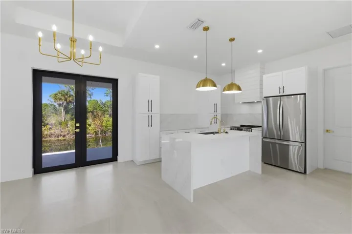 Kitchen with light stone countertops, freestanding refrigerator, a kitchen island with sink, white cabinets, and suspended lighting