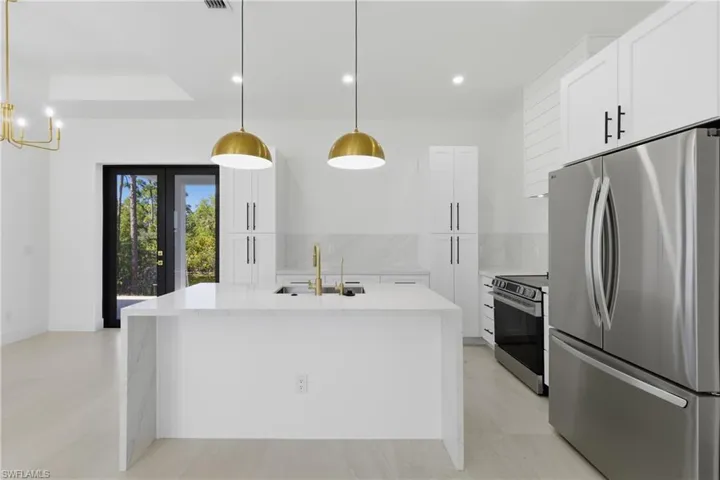 Kitchen with stainless steel appliances, light stone counters, white cabinetry, a kitchen island with sink, and backsplash