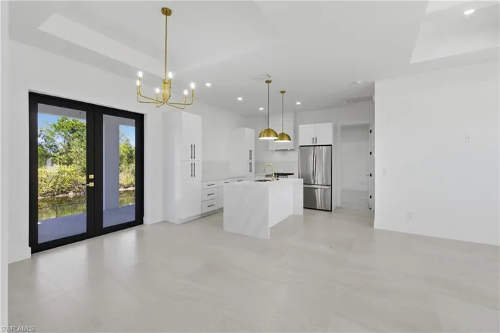 Kitchen with white cabinetry, freestanding refrigerator, french doors, light stone counters, and a tray ceiling