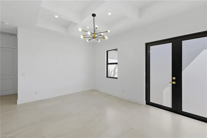 Unfurnished room featuring coffered ceiling, suspended lighting, and french doors