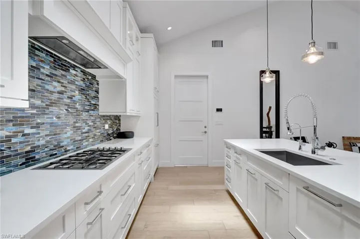 Kitchen with stainless steel gas cooktop, backsplash, light wood-style flooring, light countertops, and hanging light fixtures