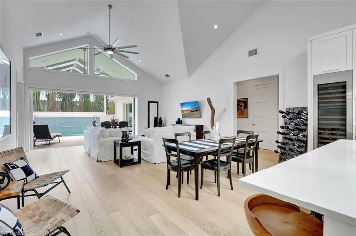 Dining room with high vaulted ceiling, wine cooler, a ceiling fan, light wood finished floors, and recessed lighting
