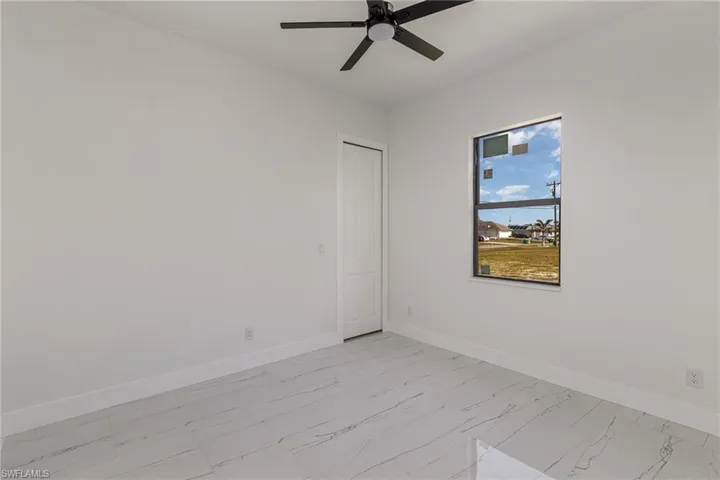 Unfurnished room featuring light marble finish floors, baseboards, and a ceiling fan