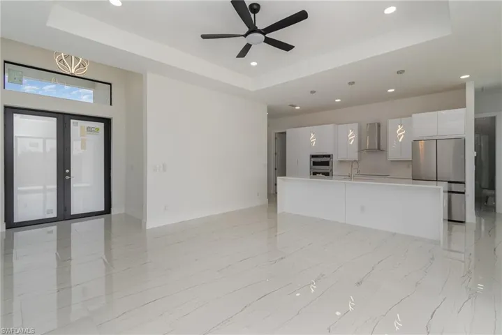 Unfurnished living room featuring a tray ceiling, recessed lighting, a ceiling fan, light marble finish floors, and baseboards