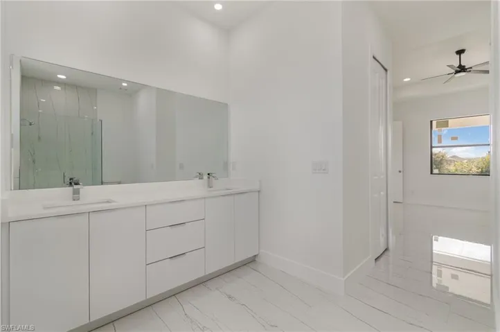 Full bathroom featuring recessed lighting, marble look tiles, baseboards, a marble finish shower, and double vanity