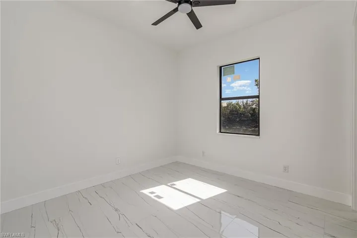 Unfurnished room featuring light marble finish floors, baseboards, and ceiling fan