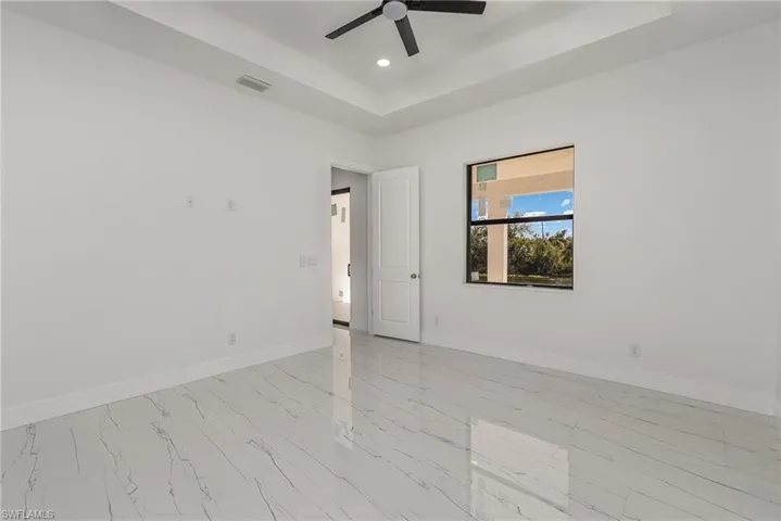 Empty room with baseboards, recessed lighting, a raised ceiling, light marble finish floors, and a ceiling fan