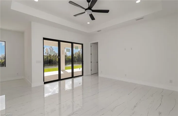 Unfurnished room with a tray ceiling, recessed lighting, baseboards, ceiling fan, and light marble finish flooring