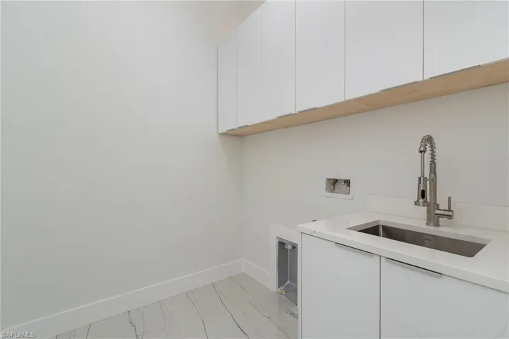 Laundry area with cabinet space, light marble finish floors, hookup for a washing machine, and baseboards
