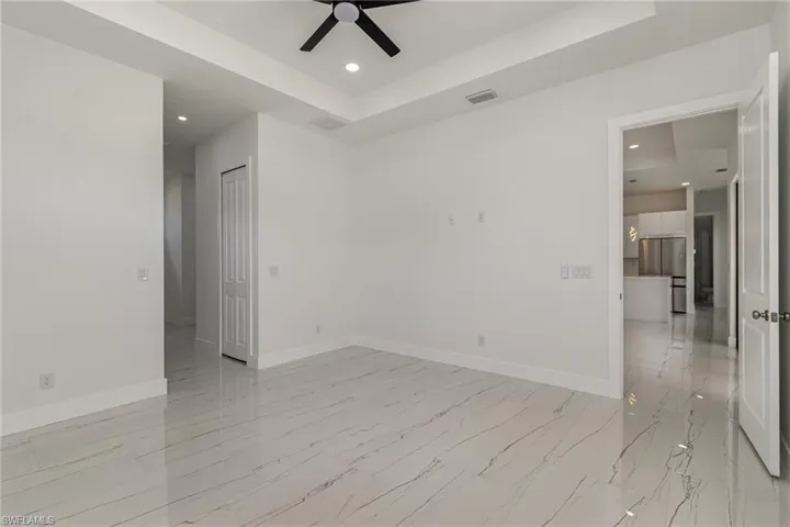 Unfurnished room with a raised ceiling, light marble finish floors, a ceiling fan, baseboards, and recessed lighting