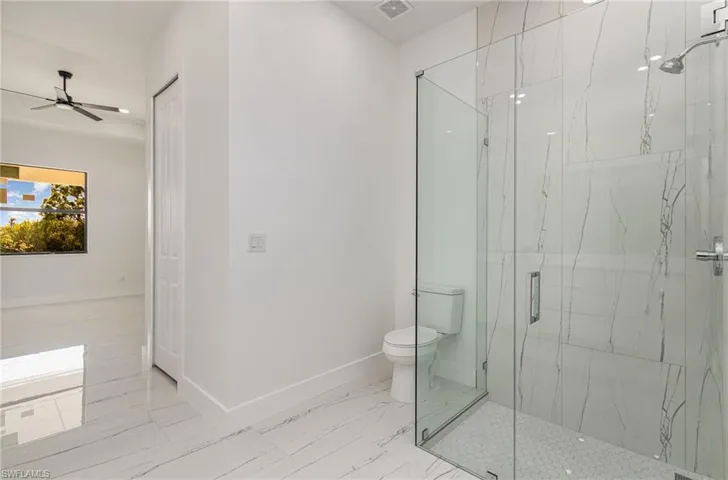Bathroom featuring toilet, a marble finish shower, baseboards, and marble finish floors