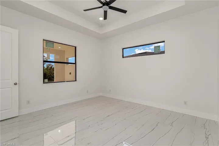 Empty room with plenty of natural light, a tray ceiling, light marble finish floors, baseboards, and recessed lighting
