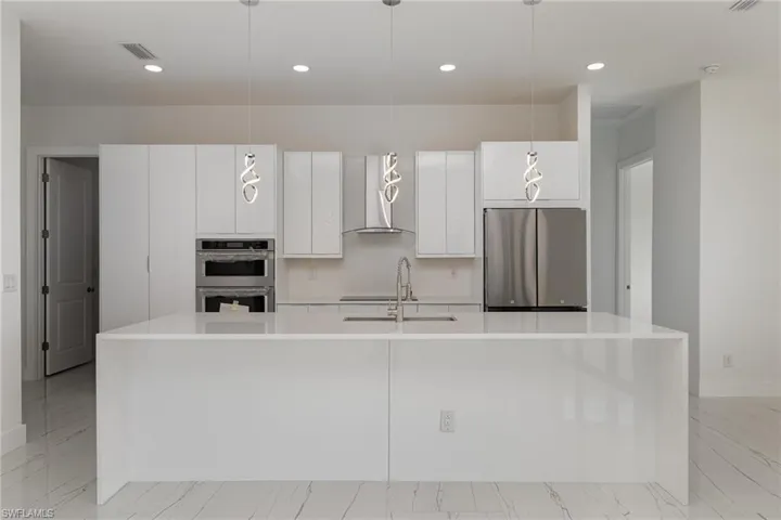 Kitchen with appliances with stainless steel finishes, a sink, wall chimney exhaust hood, light countertops, and white cabinets
