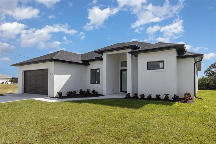 Prairie-style home with a garage, concrete driveway, stucco siding, and a front lawn