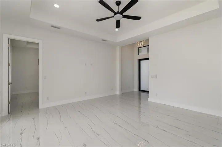 Empty room with a tray ceiling, recessed lighting, a ceiling fan, light marble finish floors, and baseboards