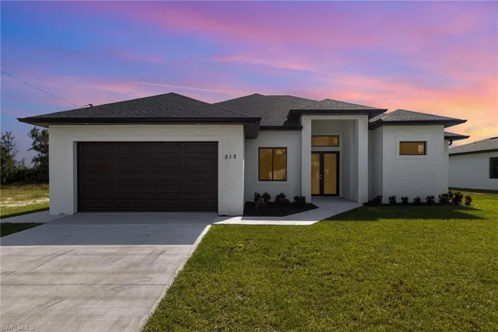 View of front of house featuring an attached garage, driveway, stucco siding, and a lawn