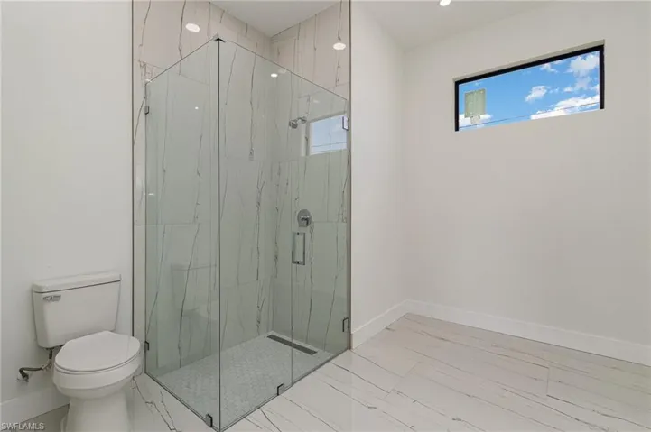 Bathroom with toilet, baseboards, a marble finish shower, and marble finish floors