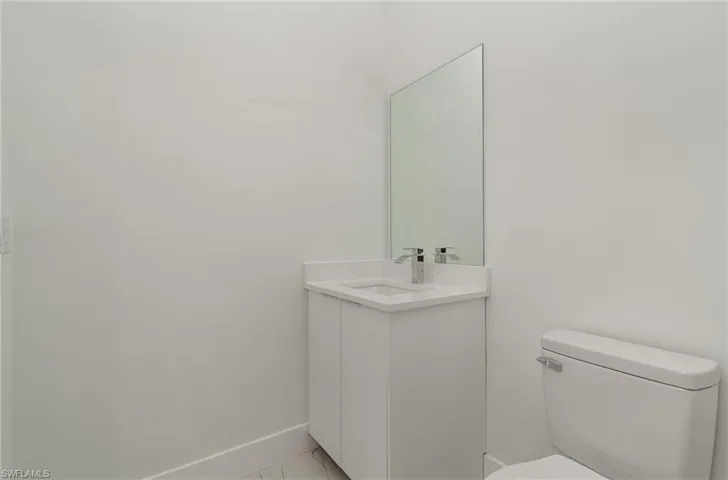 Bathroom with toilet, vanity, marble look tiles, and baseboards