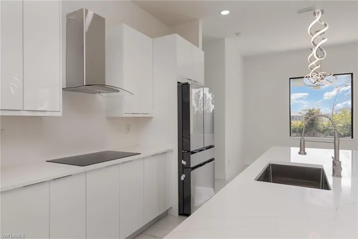 Kitchen with wall chimney range hood, a sink, black electric stovetop, modern cabinets, and white cabinetry