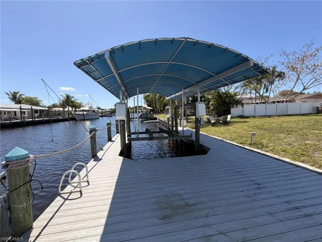 Dock with boat lift, a water view, and a lawn