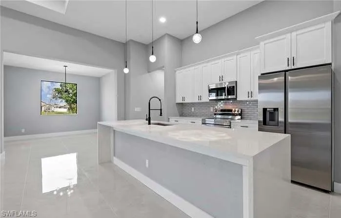 Kitchen featuring appliances with stainless steel finishes, decorative light fixtures, and an island with sink