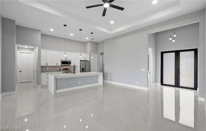 Kitchen featuring appliances with stainless steel finishes, an island with sink, ceiling fan, pendant lighting, and white cabinets