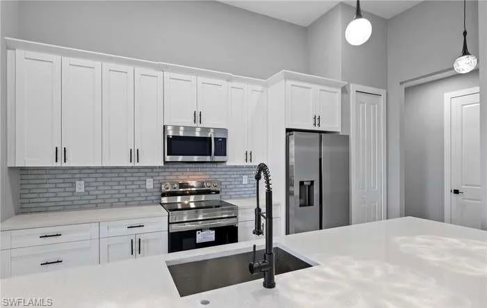 Kitchen featuring sink, appliances with stainless steel finishes, decorative light fixtures, and white cabinetry
