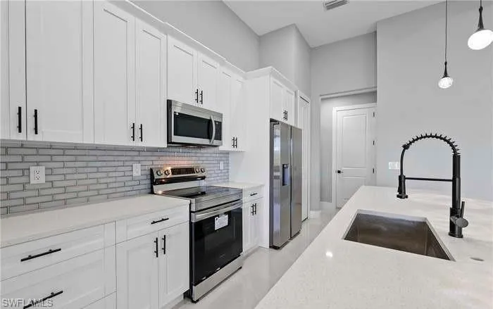 Kitchen with decorative backsplash, stainless steel appliances, sink, pendant lighting, and white cabinets