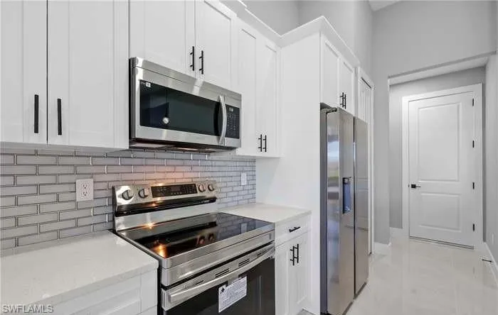 Kitchen with appliances with stainless steel finishes, decorative backsplash, white cabinets, and light tile patterned flooring
