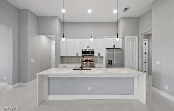 Kitchen featuring sink, white cabinetry, stainless steel appliances, pendant lighting, and a kitchen island with sink