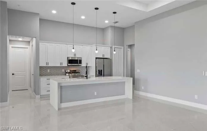 Kitchen with white cabinetry, a kitchen island with sink, a towering ceiling, decorative light fixtures, and stainless steel appliances