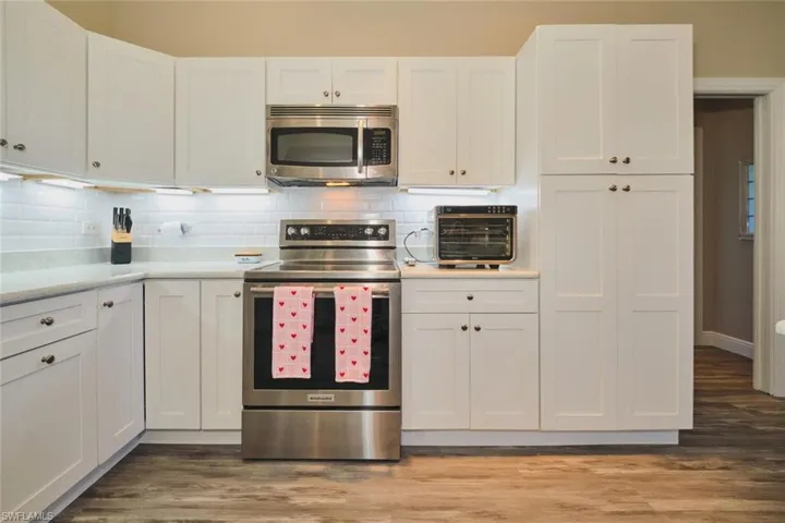 Kitchen with stainless steel appliances, white cabinets, decorative backsplash, and dark wood finished floors