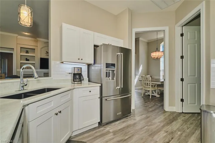 Kitchen with hanging light fixtures, white cabinets, ornamental molding, stainless steel appliances, and light wood-style floors