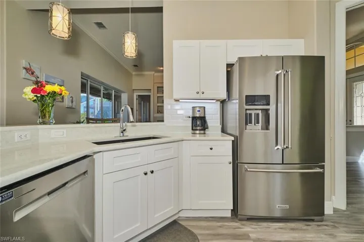 Kitchen featuring stainless steel appliances, white cabinets, light wood finished floors, decorative backsplash, and pendant lighting