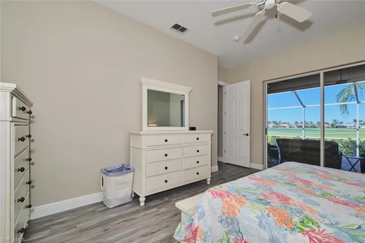 Bedroom with dark wood finished floors, access to exterior, view of golf course, and a ceiling fan