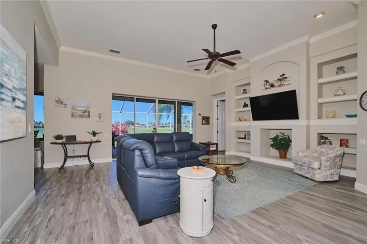 Living room featuring built in shelves, a ceiling fan, light wood-type flooring, and ornamental molding