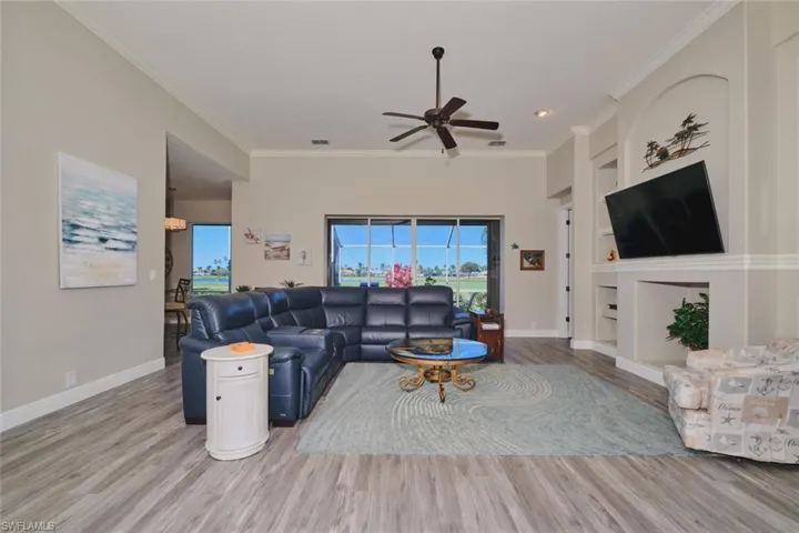 Living room with built in features, ceiling fan, light wood-style floors, and ornamental molding