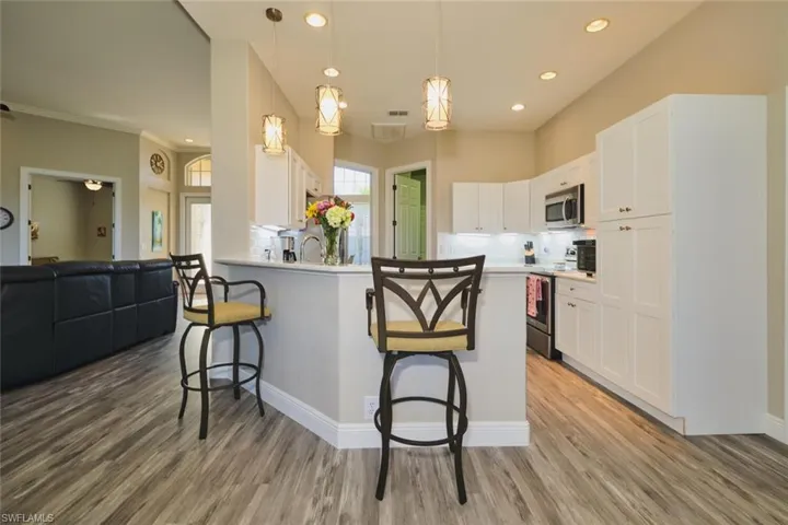 Kitchen featuring white cabinetry, a breakfast bar area, decorative light fixtures, stainless steel appliances, and a peninsula