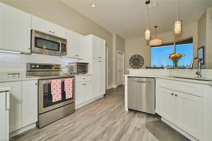 Kitchen with stainless steel appliances, white cabinets, pendant lighting, light wood-style flooring, and light stone countertops