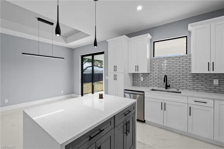 Kitchen with sink, dishwasher, light stone counters, a tray ceiling, and white cabinets