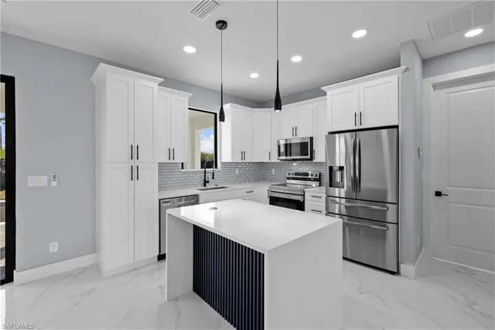 Kitchen with sink, a center island, hanging light fixtures, stainless steel appliances, and white cabinets