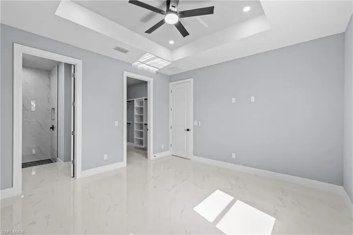 Unfurnished bedroom featuring ensuite bath, a walk in closet, a tray ceiling, a closet, and ceiling fan